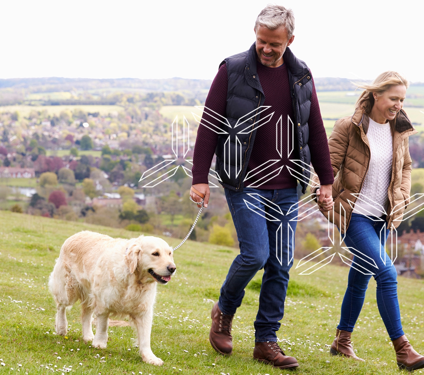 Man and woman wearing fall clothing walk golden retriever with mountains in background